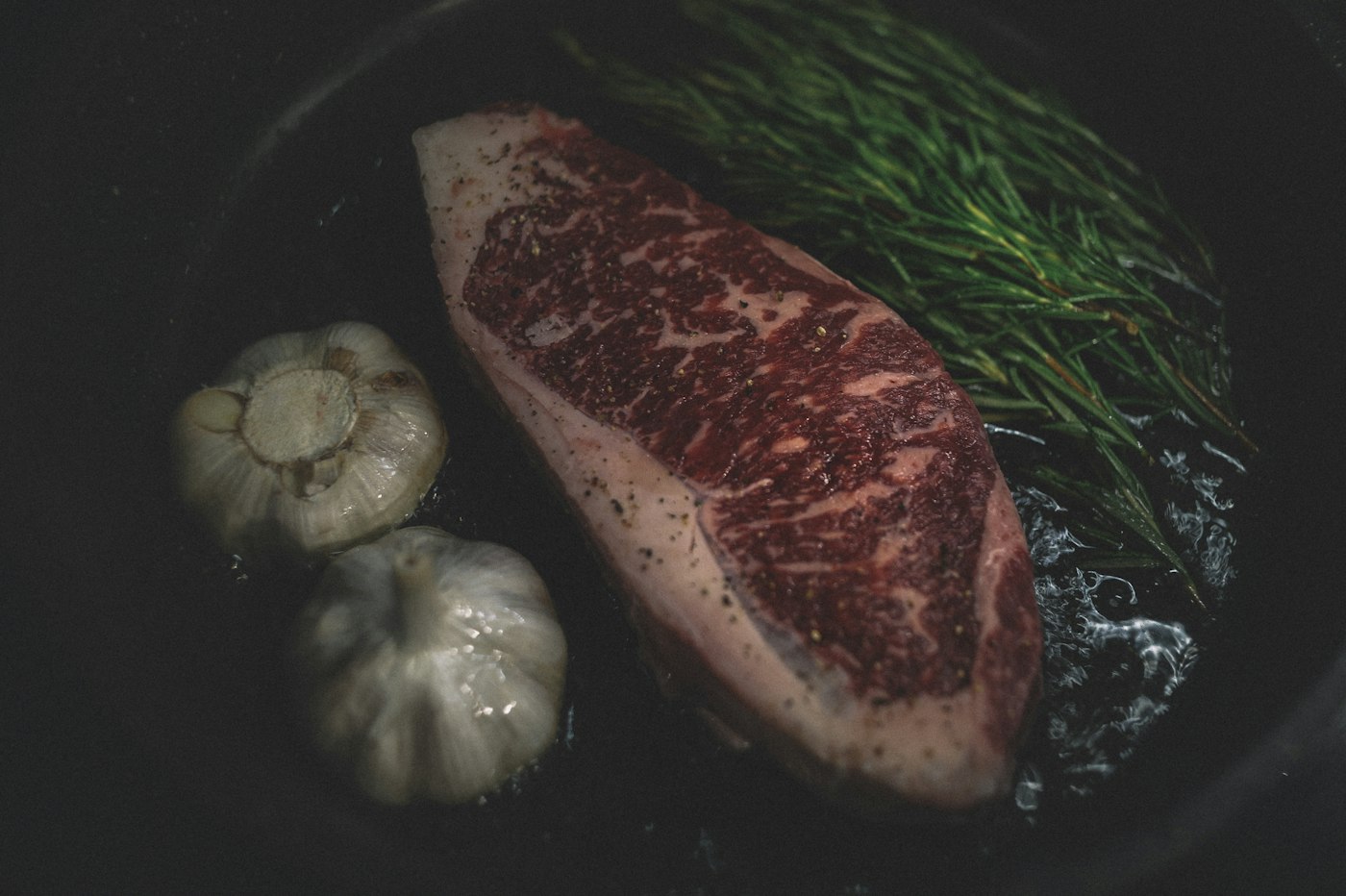 A raw marbled sirloin steak with garlic and rosemary
