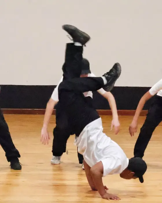 Boys in white t-shirts and caps, one balanced upside down in a breakdance freeze.