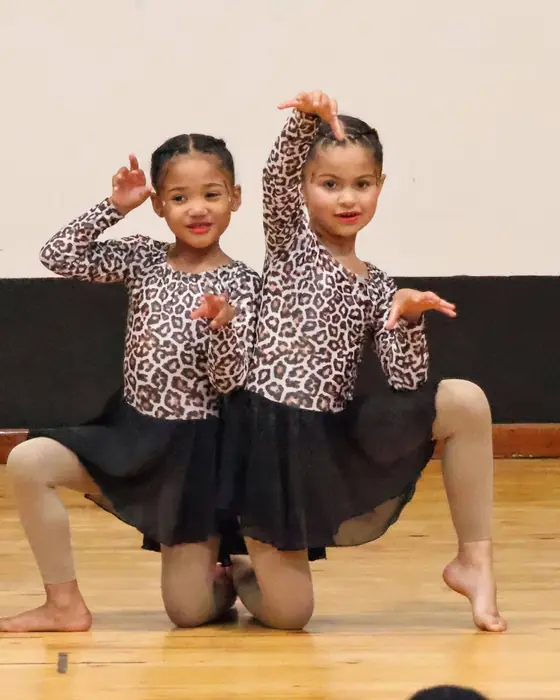 Two small dancers in leopard print kneel on stage with their hands up like claws.