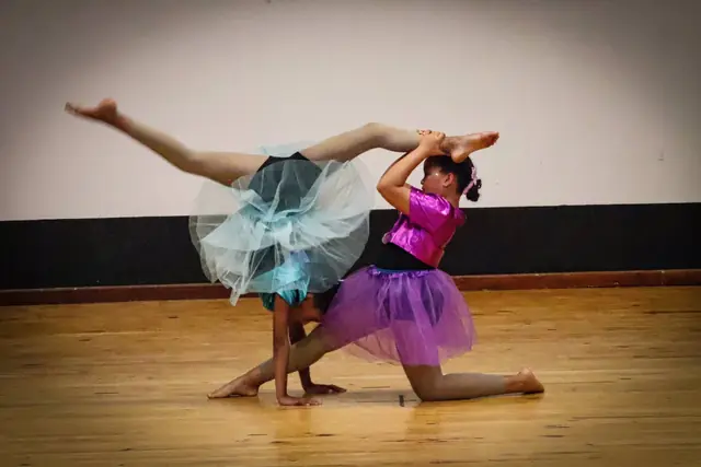 Two young dancers in tutus, one in a deep backbend over the other.