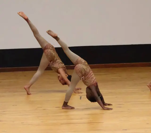 Two dancers in gold costumes doing cartwheels across the stage.