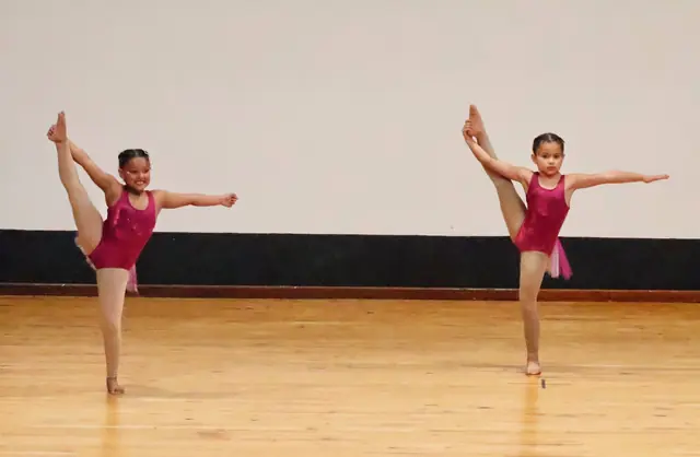 Two dancers in pink holding a high leg extension at the side.