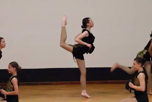 A dancer kicking one leg high in a black costume during a group piece.