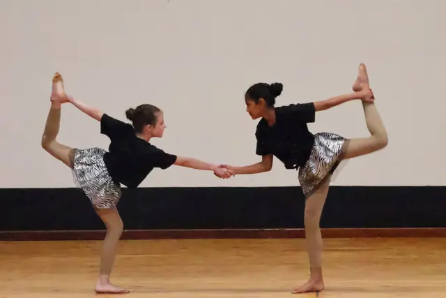 Two dancers holding hands, each balancing with a foot pulled up behind.
