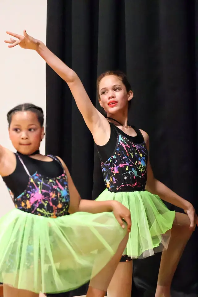 Two dancers in sparkly tops and neon green tutus, one with her arm raised.