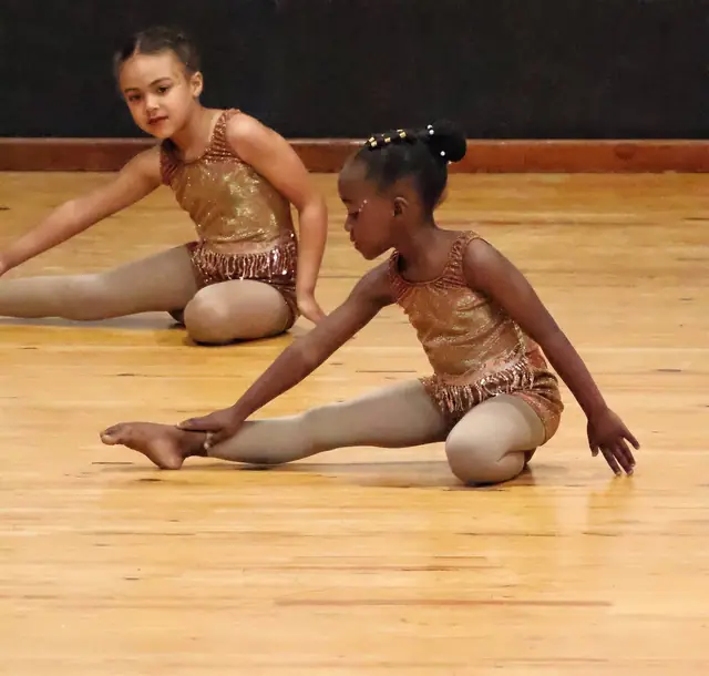 Two young dancers stretching forward on the stage floor.