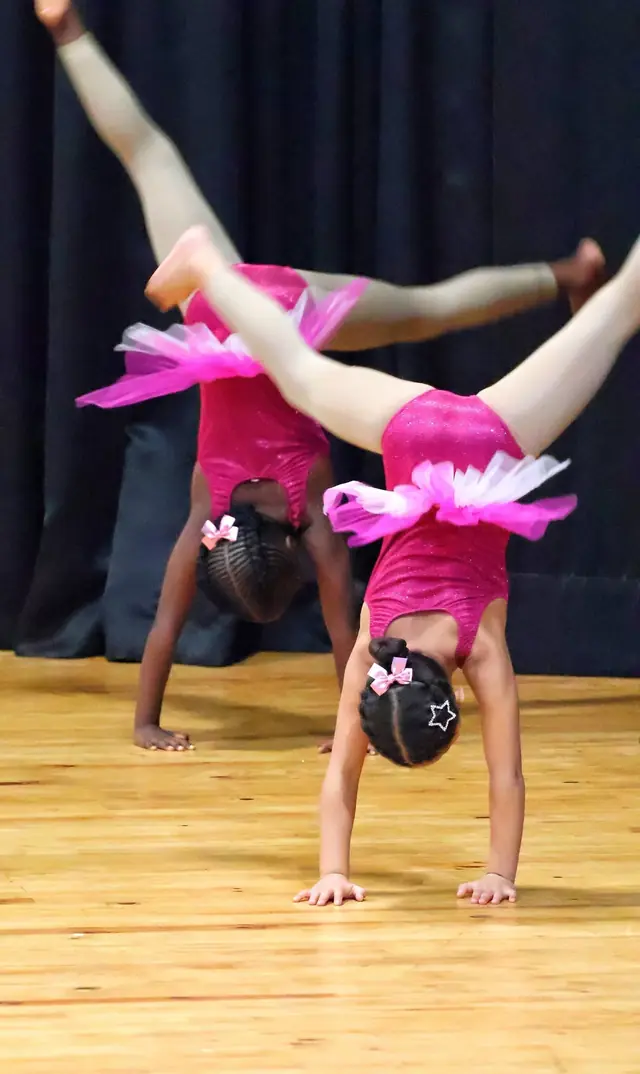 Two little dancers in pink tutus doing handstands side by side.