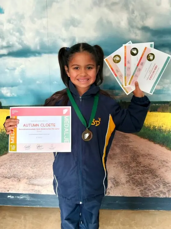 A young dancer smiling with her medal and a fan of eisteddfod certificates.