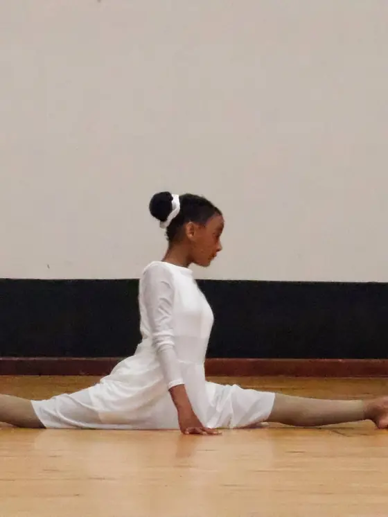 A dancer in a white dress in a full split on the stage floor.