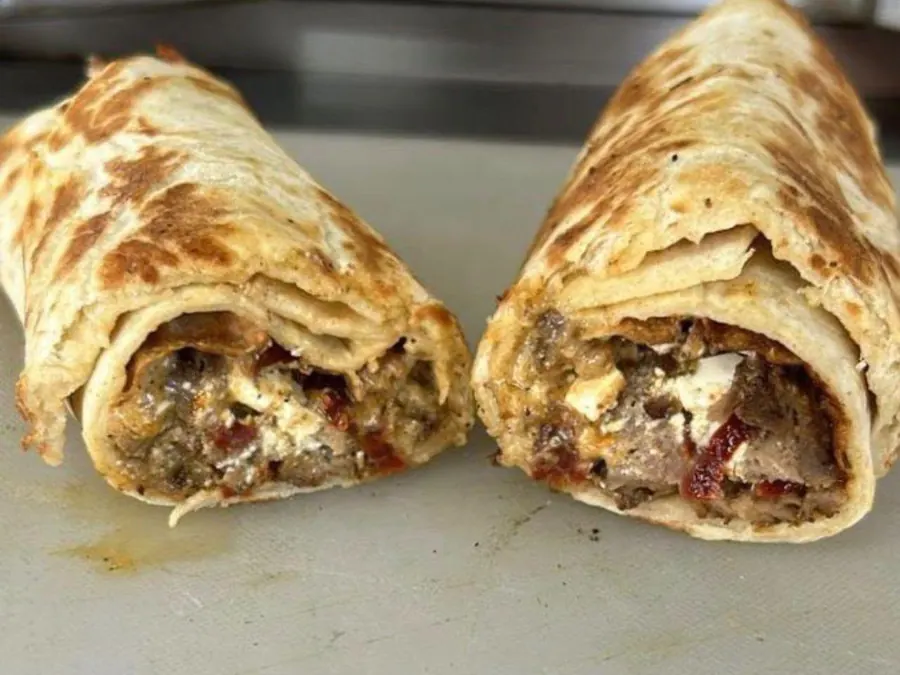 Two halves of a grilled shawarma wrap stuffed with beef, cheese and peppers