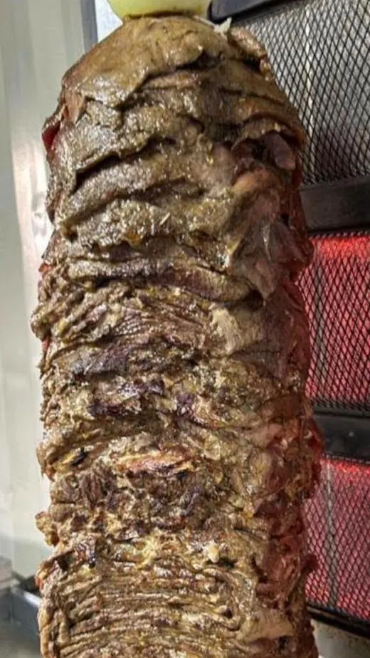 A tall shawarma spit of seasoned meat turning in front of the grill